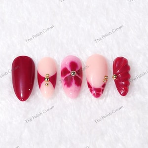May include: A set of five artificial nails with various designs. The nails feature colors like burgundy, pink, and nude, with accents of gold beads and floral patterns. The text "The Polish Crown" is visible.