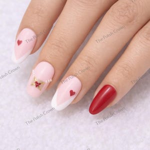 May include: A hand with manicured nails. Some nails are painted light pink with white tips and red hearts. One nail is solid red. The Polish Crown is printed on the background.
