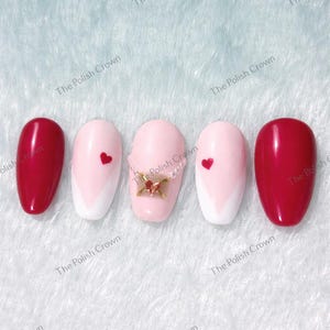 May include: Five artificial nails with a variety of designs. Two nails are a solid, glossy red. Two nails are light pink with a white chevron design and a red heart. The center nail is light pink with a gold charm. The text "The Polish Crown" is visible.