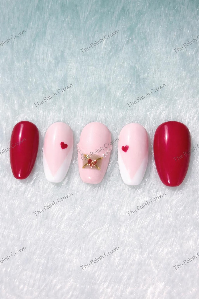 May include: Five artificial nails with a variety of designs. Two nails are a solid, glossy red. Two nails are light pink with a white chevron design and a red heart. The center nail is light pink with a gold charm. The text "The Polish Crown" is visible.