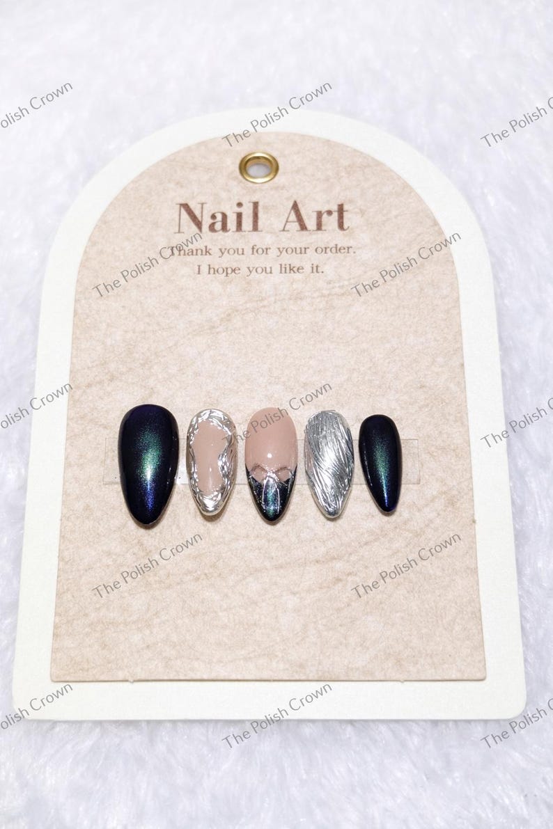 May include: A set of five artificial nails with various designs. The nails feature colors like navy, silver, and nude, with some adorned with intricate silver and iridescent accents. The card reads "Nail Art" and "Thank you for your order. I hope you like it."