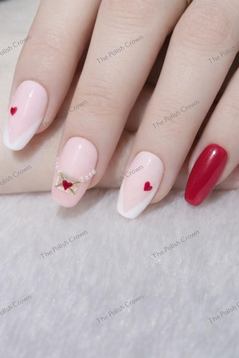 May include: A hand with manicured nails. Some nails are light pink with white tips and red hearts. One nail features a small envelope design with a heart. Another nail is solid red.