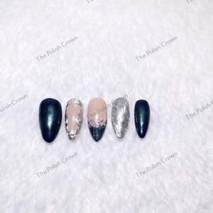 May include: Five artificial nails in a row, each with a different design. The nails are oval-shaped and feature colors like dark teal, silver, and nude. Some nails have glitter or decorative elements. The Polish Crown is printed on the background.