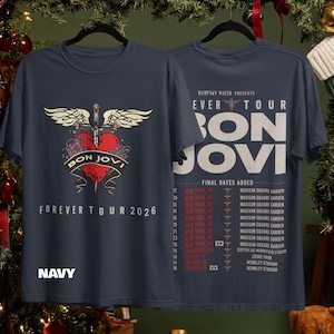 May include: A navy blue t-shirt featuring a graphic of a red heart pierced by a sword with wings on the front, and the text Bon Jovi Forever Tour 2026. The back displays tour dates and venues for the Hampton Water Presents Forever Tour.