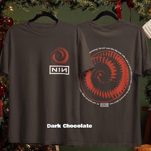 May include: Dark chocolate-colored t-shirt featuring a red spiral design and the text "NIN" in a white box. The back of the shirt has a matching spiral design and text. The shirt is displayed on a black hanger.