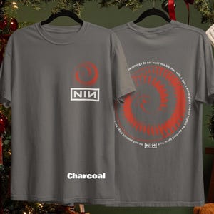 May include: Charcoal gray t-shirts with a red spiral design and the text "NIN". One shirt displays the NIN logo and a red circle. The other shirt has a spiral design and text. The word "Charcoal" is printed on the front.