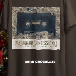 May include: Dark chocolate-colored t-shirt featuring a distressed image of a cassette tape. Below the image is the text "DASHBOARD CONFESSIONAL" and the words "A MARK &bull; A MISSION &bull; A BRAND &bull; A SCAR". The text "DARK CHOCOLATE" is printed at the bottom.