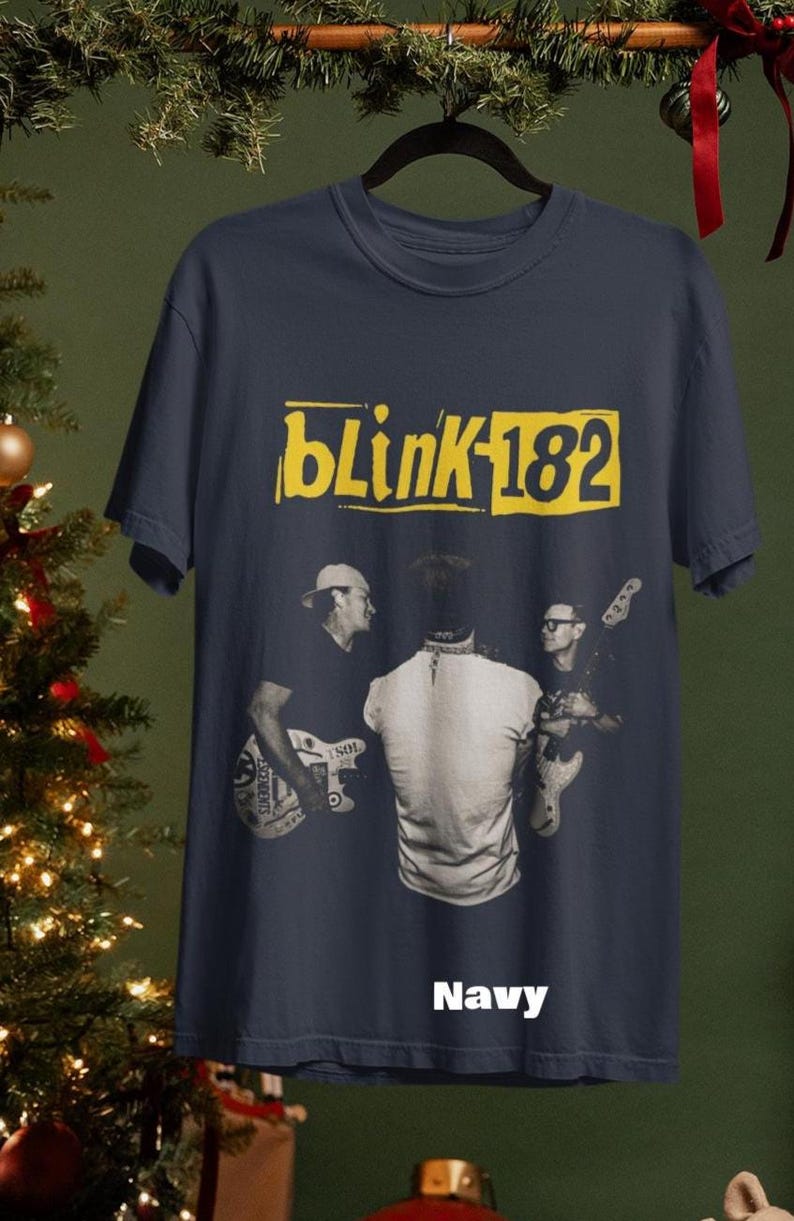 May include: Navy blue t-shirt featuring the band Blink-182's logo in yellow. The shirt has a graphic of the band members playing instruments. The word "Navy" is printed at the bottom of the shirt.