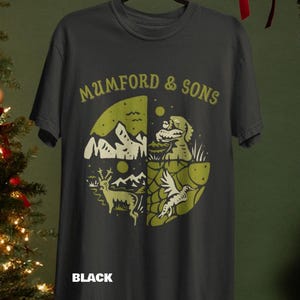 May include: Black t-shirt featuring a circular design with a mountain range, deer, and other nature-themed illustrations in olive green. The text "MUMFORD & SONS" arches above the design. The word "BLACK" is printed below the design.