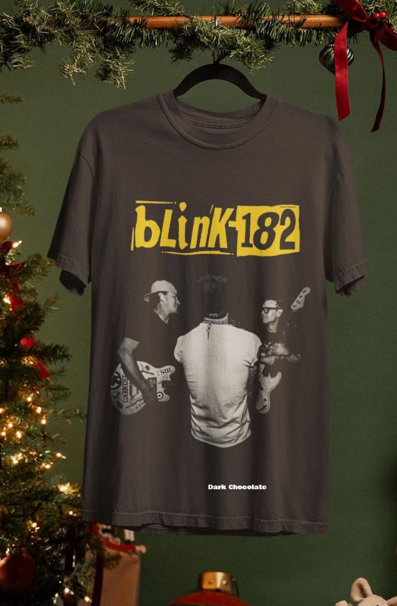 May include: Dark chocolate t-shirt featuring the band Blink-182. The shirt has a yellow rectangular logo with the band's name and number. A black and white image of the band members playing their instruments is on the front.