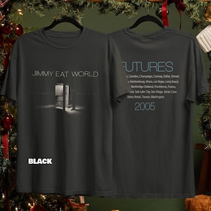 Puede incluir: Una camiseta negra de manga corta con el texto Jimmy Eat World y un gráfico de una cabina telefónica en el frente. La parte posterior muestra el texto Futures, una lista de nombres de ciudades y el año 2005 en letras azul claro sobre la tela oscura.