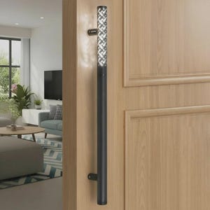 Pode incluir: Um puxador de porta cilíndrico vertical preto mate montado numa porta de madeira clara. A secção superior do puxador apresenta um padrão de corte decorativo com um interior branco, enquanto a inferior é um tubo preto sólido.