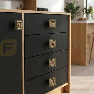 May include: A set of square cabinet knobs featuring a metallic gold finish with an intricate, openwork geometric lattice pattern. These knobs are mounted on matte black drawer fronts with light wood trim, providing a distinct contrast.