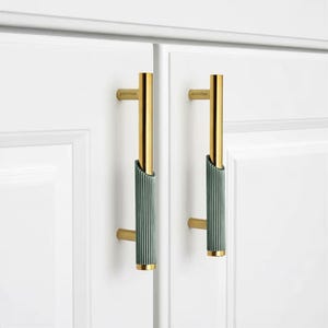 May include: Two vertical cabinet pulls mounted on white doors. Each handle features a smooth, polished gold-tone upper section and a textured, dark green ribbed lower section. The word "plantex" is engraved on the gold portion of each handle.