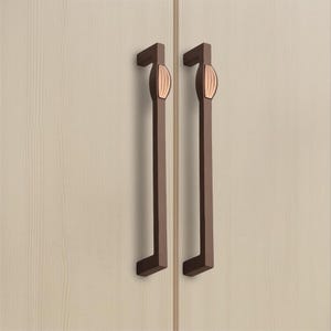 Puede incluir: Dos tiradores de armario verticales de color marrón oscuro con perfil rectangular y una pieza central redondeada de color cobre claro con estrías verticales. Los tiradores están montados uno al lado del otro sobre una superficie de madera clara.