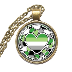 Op de afbeelding: Een ketting met een ronde hanger met een groen, wit en zwart hart in een glas-in-lood stijl. De hanger is omgeven door een gouden rand.