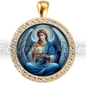 May include: Gold-coloured pendant featuring an angel in blue robes, holding a glowing orb. The round pendant is surrounded by clear crystals. The pendant has a gold bail for attaching to a chain. The image has the text "Picture Vale Atelier".