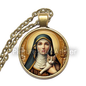 Op de afbeelding: Een ronde hangerketting met een bronzen ketting. De hanger toont een portret van een vrouw met een donkerblauwe sluier die een kat vasthoudt. De achtergrond is goudkleurig met bloemmotieven. De tekst "Picture Rescue Atelier" is zichtbaar.
