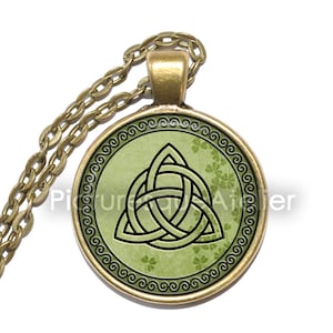 Puede incluir: Un collar de cadena dorada con un colgante redondo que presenta un diseño de nudo celta verde con un fondo de patrón de trébol verde.