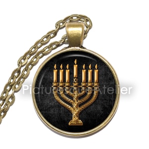 May include: A gold menorah necklace pendant with seven candles on a black background. The menorah is a traditional Jewish symbol.