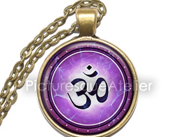May include: A round pendant necklace with a gold-colored chain. The pendant features a purple background with the Om symbol in black. The pendant is framed with a gold-colored metal.