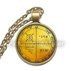 May include: A gold pendant necklace with a round, yellow glass charm featuring Hebrew text and symbols. The charm is surrounded by a silver-colored metal frame.
