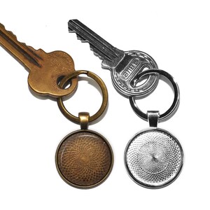 May include: Two keychains with round, decorative glass charms. One charm is bronze with a swirling pattern, the other is silver with a similar pattern. Both keychains are attached to keys.