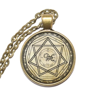 Può includere: Una collana con un ciondolo rotondo in vetro dorato, che presenta un'illustrazione in bianco e nero di uno scorpione all'interno di una stella di David. Il ciondolo è circondato da testo ebraico.