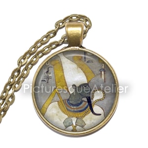 May include: A gold chain necklace with a round glass pendant featuring a colorful image of an Egyptian god with a white headdress and a blue face.