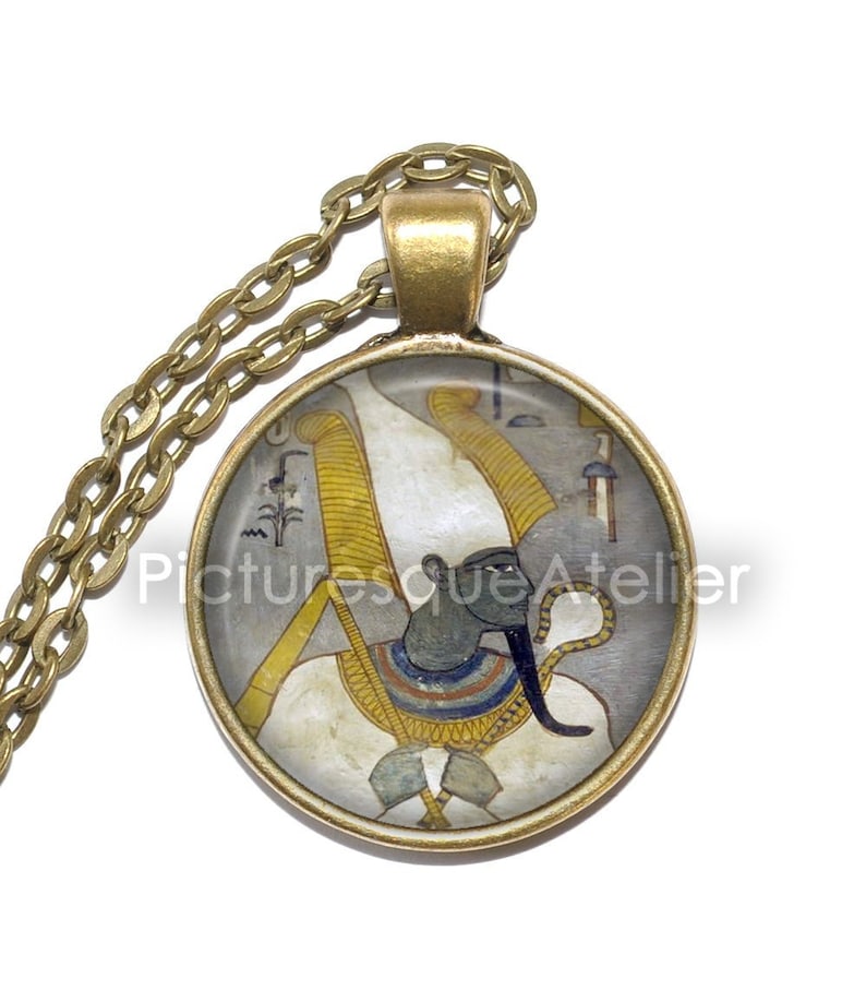 May include: A gold chain necklace with a round glass pendant featuring a colorful image of an Egyptian god with a white headdress and a blue face.