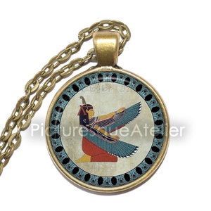 May include: A gold chain necklace with a round pendant featuring a colorful image of the Egyptian goddess Isis with outstretched wings. The pendant has a black background with a blue and gold border.