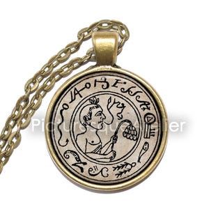 May include: A gold chain necklace with a round pendant featuring a black and white illustration of a person holding a flower. The pendant has a gold rim and the text "E.I.S.S.A.O.I" around the edge.