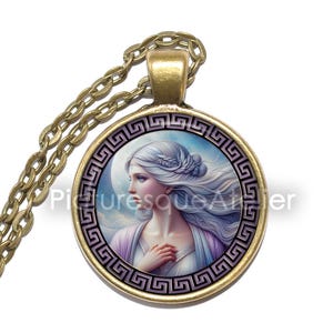 Può includere: Collana con pendente rotondo e catena dorata. Il pendente presenta un ritratto di donna con capelli bianchi fluenti, incorniciato da un motivo a chiave greca nero e oro. La donna indossa un abito bianco e lavanda.