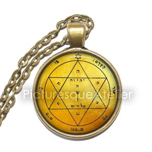 Può includere: Una collana con un ciondolo rotondo in vetro giallo, decorato con un'iscrizione ebraica e una stella a sei punte. Il ciondolo è circondato da una cornice in metallo dorato.