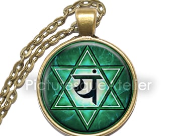 May include: A green and gold necklace with a round pendant featuring a green and white star of David with the Sanskrit symbol "Ya" in the center. The pendant is surrounded by a gold rim.