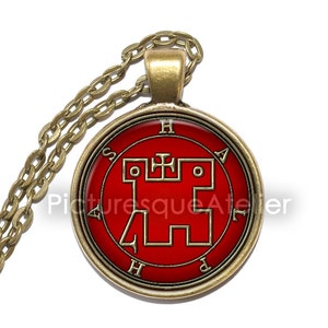 May include: A gold chain necklace with a round pendant featuring a red background and a gold sigil. The sigil is a geometric design with a cross in the center. The pendant is surrounded by a gold frame with the letters "H", "A", "P", and "S" around the edge.