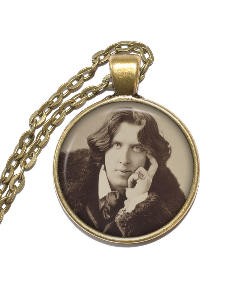May include: A gold chain necklace with a round pendant featuring a black and white portrait of a man with long hair. The man is wearing a dark jacket and has his hand resting on his chin.