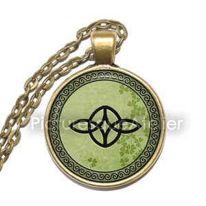 May include: A gold chain necklace with a round pendant featuring a Celtic knot design in black on a green background with a shamrock pattern. The pendant has a gold border with a decorative swirl pattern.