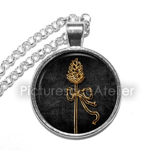 May include: A silver chain necklace with a round pendant featuring a gold stylized image of a wheat stalk with a bow on a black background.