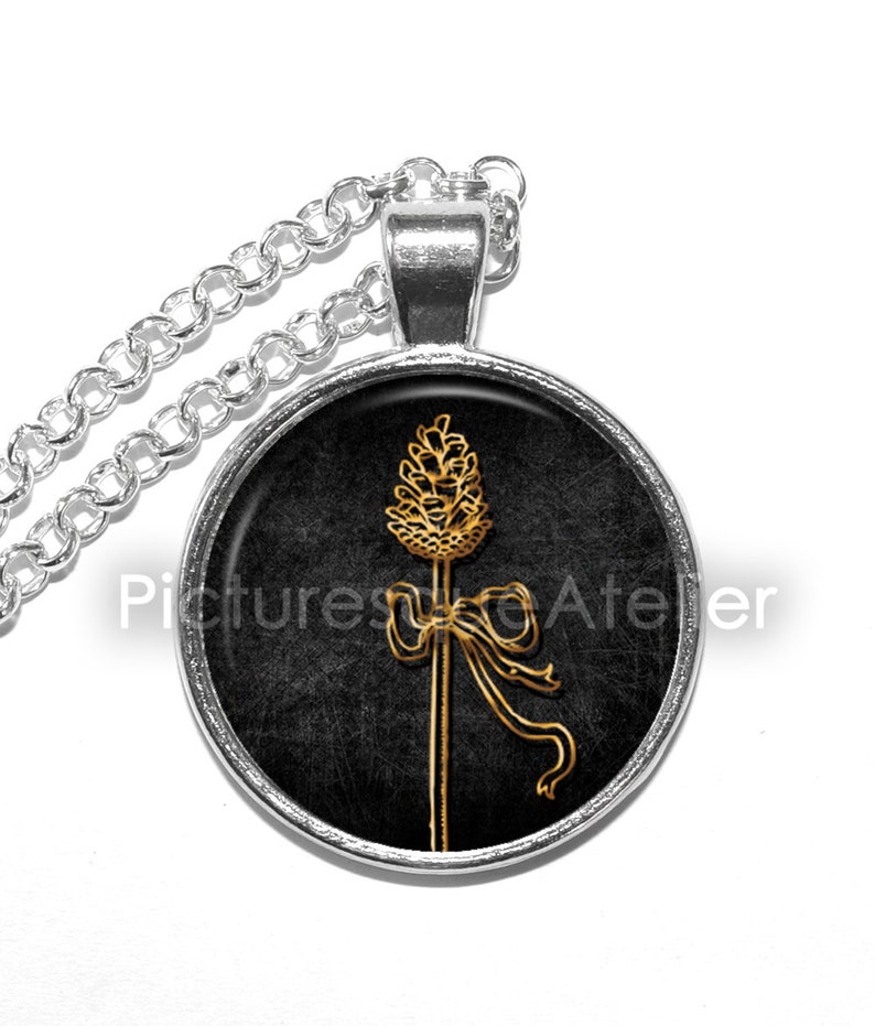May include: A silver chain necklace with a round pendant featuring a gold stylized image of a wheat stalk with a bow on a black background.
