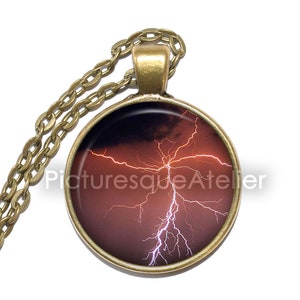 May include: A bronze chain necklace with a round pendant featuring a photograph of a lightning bolt striking during a thunderstorm. The pendant has a dark red background with a white lightning bolt.