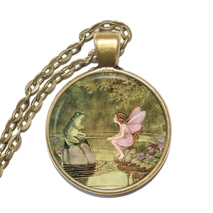 May include: A bronze necklace with a round glass pendant featuring a fairy with pink wings sitting on a rock by a pond, talking to a green frog on a rock.