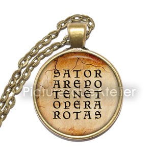May include: A bronze necklace with a round pendant featuring a vintage-style image of the Sator Square, a Latin word square palindrome. The pendant has a cracked, aged look and the words are in black.