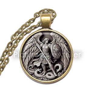 May include: A round pendant necklace featuring an angel slaying a dragon. The pendant has a gold-coloured frame and chain. The angel is shown with wings, a shield, and a sword. The background is dark, and the design is highly detailed.