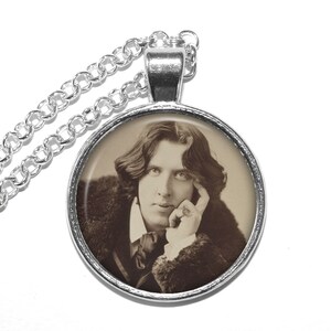 May include: A silver chain necklace with a round pendant featuring a black and white photograph of a man with long hair. The man is wearing a dark jacket and has his hand resting on his chin.