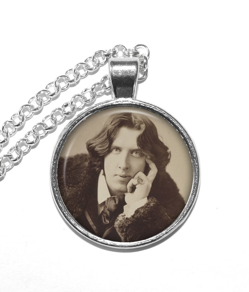 May include: A silver chain necklace with a round pendant featuring a black and white photograph of a man with long hair. The man is wearing a dark jacket and has his hand resting on his chin.
