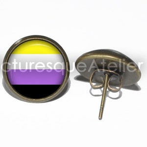 May include: A pair of bronze stud earrings with a round glass cabochon featuring the non-binary pride flag. The flag has yellow, white, purple, and black horizontal stripes.