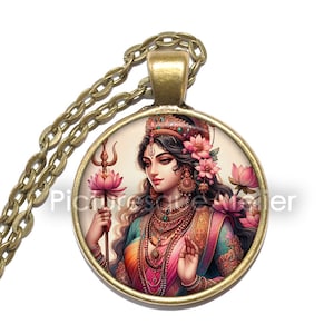 May include: A gold necklace with a round pendant featuring a colorful illustration of a Hindu goddess with flowers in her hair. The pendant is surrounded by a gold frame.
