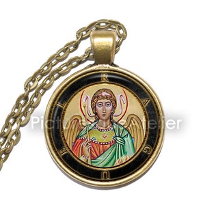 May include: A gold chain necklace with a round pendant featuring a colorful icon of an angel with wings and a halo. The pendant has a black border with gold lettering that reads "LIRAUG".