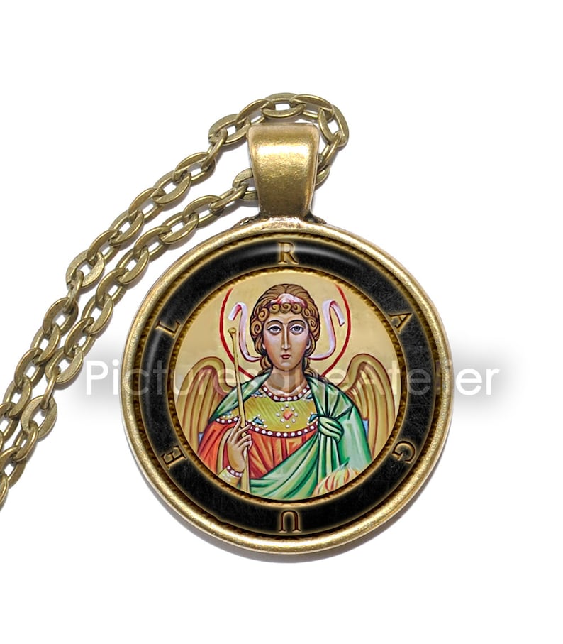 May include: A gold chain necklace with a round pendant featuring a colorful icon of an angel with wings and a halo. The pendant has a black border with gold lettering that reads "LIRAUG".
